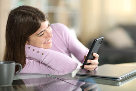 Happy teen watching content on phone sitting at homeの写真素材