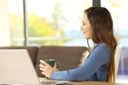 Profile of a relaxed woman thinking and looking away sitting on a chair at homeの写真素材