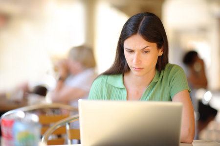 Front view portrait of a suspicious woman using laptop in a restaurant terraceの写真素材