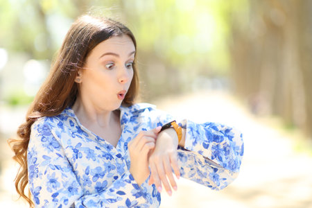 Surprised woman checking smartwatch walking in a parkの写真素材