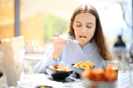 Front view portrait of a woman eating tapas in a bar terrace aloneの写真素材