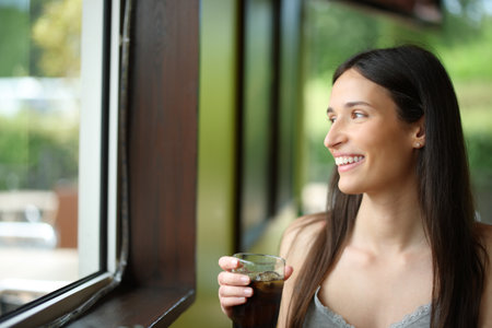 Happy woman sitting in a coffee shop drinking soda and smilingの写真素材