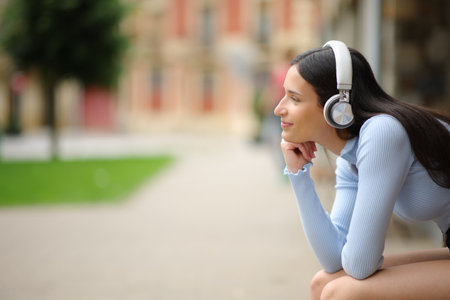 Profile of a woman wearing headphone relaxing and contemplating sitting on a bench listening to audio in the streetの写真素材