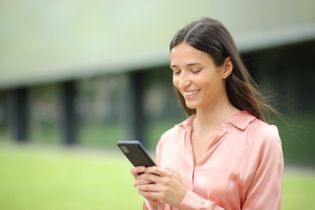 Single happy woman using cell phone walking in a parkの写真素材