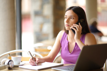 Serious student studying and talking on phone in a restaurant terraceの写真素材