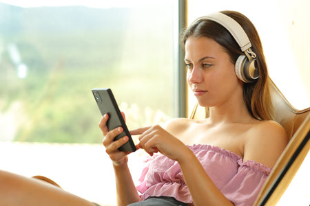 Teen listening music on a chair using phone and headphone at homeの写真素材