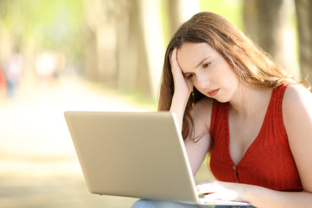 Worried female checking laptop sitting in a parkの写真素材