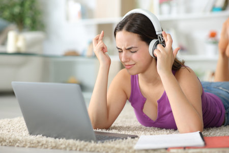 Stressed student crossing fingers expecting online results in a laptop at homeの写真素材