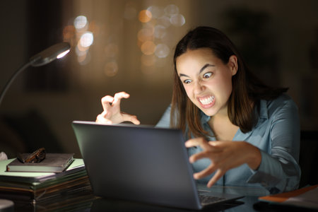 Angry teleworker using laptop in the night at homeの写真素材