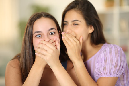Woman sushing a secret to the ear of a surprised friend at homeの写真素材
