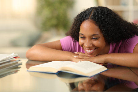 Happy black woman reading paper book on a desk at homeの写真素材