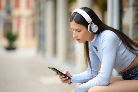 Woman listening audio with headphones and phone sitting in the streetの写真素材
