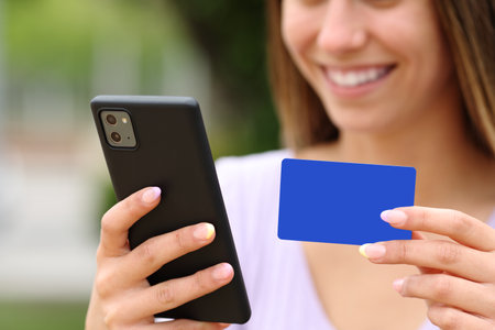 Close up of a happy teen hands buying online with credit card and smart phone outdoorsの写真素材