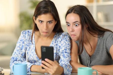 Perplexed women checking cell phone content sitting at homeの写真素材