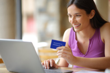 Happy buyer with laptop and credit card buying online in a restaurant terraceの写真素材