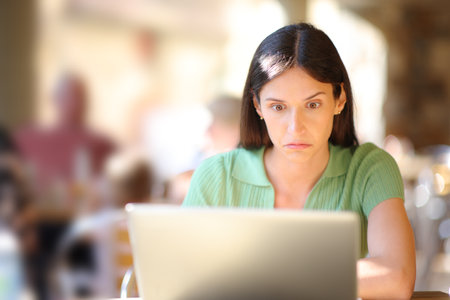 Front view portrait of a perplexed woman checking laptop in a restaurantの写真素材