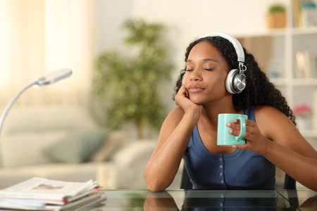 Black woman wearing headphone relaxing listening music drinking coffee at homeの写真素材