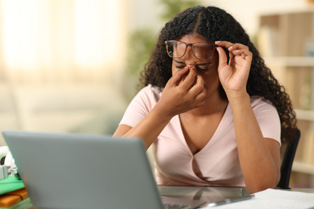 Black student suffering eyestrain studying with a laptop at homeの写真素材
