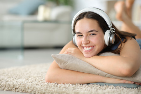 Happy woman looks at you wearing headphone lying on the floor at homeの写真素材