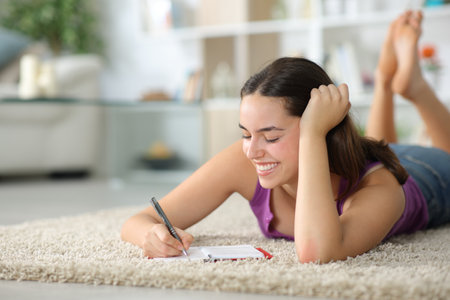 Happy woman taking notes in agenda lying on a carpet at homeの写真素材