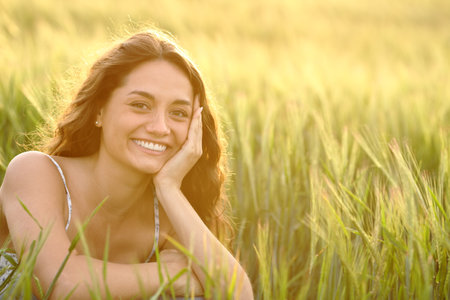Portrait of a happy woman in wheat field smiling at camera at sunsetの写真素材