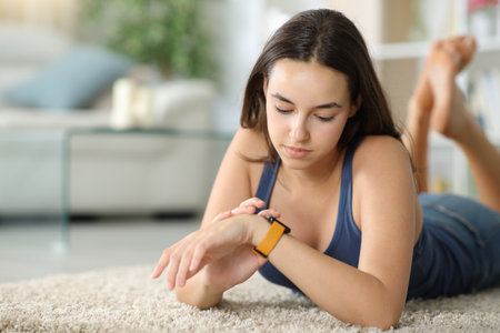 Woman checking smartwatch lying on the floor at homeの写真素材
