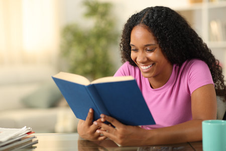 Happy black woman reading a paper book sitting at homeの写真素材