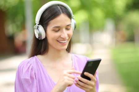 Happy woman listening to music on cell phone walking in a parkの写真素材