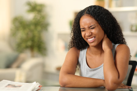 Black woman suffering neck ache sitting on a chair at homeの写真素材