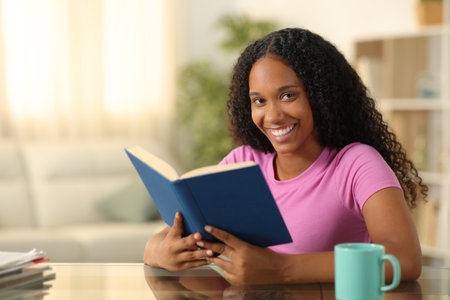 Happy black reader looking at camera holding paper book at homeの写真素材