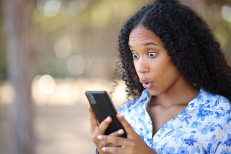 Amazed black woman checking surprising content on phone in a park