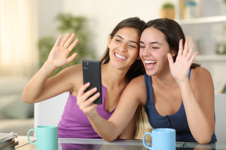 Two happy roommates having video call on phone at homeの写真素材