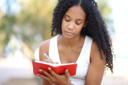 Front view portrait of a black woman writing in agenda on the beachの写真素材