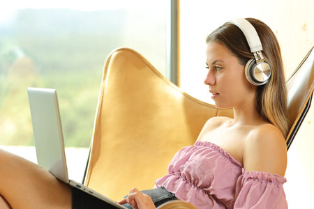 Profile of a woman using laptop and headphone on a chair at homeの写真素材