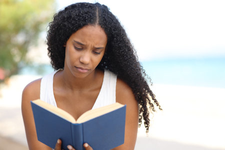 Front view of a serious black woman reading a paper book on th beachの写真素材
