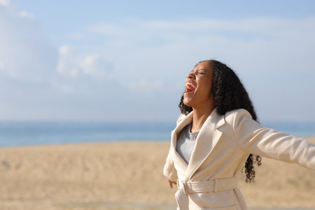 Happy black woman on the beach screaming to the air in winter a sunny dayの写真素材