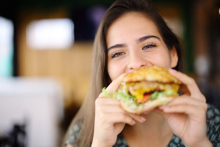 Happy woman eating burger looking at you in a restaurantの写真素材