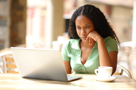 Serious black woman checking laptop in a bar terraceの写真素材
