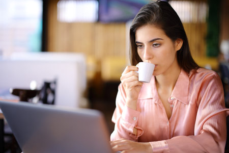 Serious woman using laptop drinking coffee in a bar interiorの写真素材