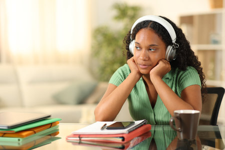 Distracted black student wearing headphone looking at side at homeの写真素材