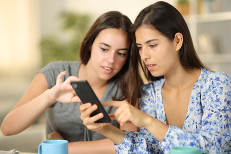 Friends talking about phone content at homeの写真素材