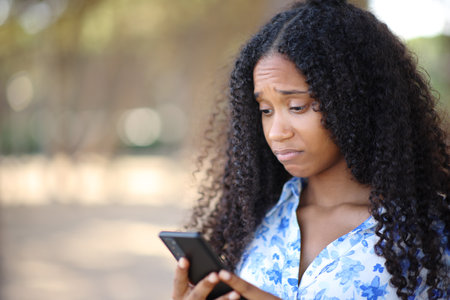 Disappointed black woman checking cell phone in a parkの写真素材