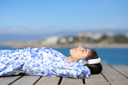 Profile of a relaxed woman on the beach listening audio with wireless headphoneの写真素材