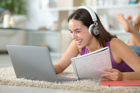 Happy student e-learning using headphone and laptop lying on the floor at homeの写真素材