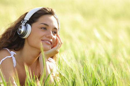 Relaxed woman listening music with headphones in a green fieldの写真素材