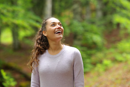Happy casual woman looking up amazed walking in a forestの写真素材
