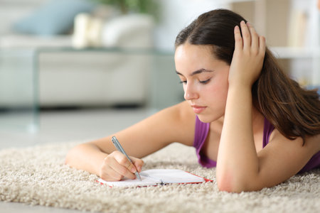Woman writing in agenda lying on the floor at homeの写真素材