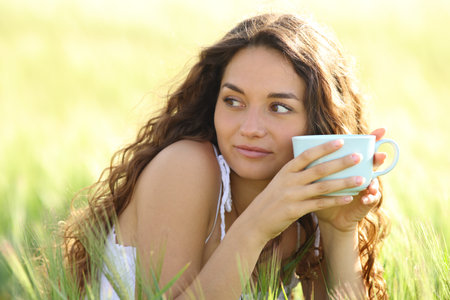 Woman drinking coffee looking at side sitting in a fieldの写真素材