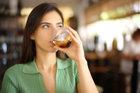 Serious woman drinking soda in a restaurant interior looking at side