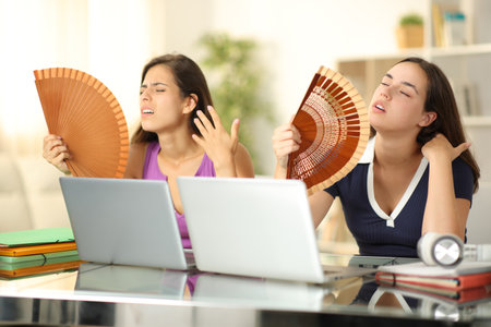 Two overwhelmed students fanning suffering heatwave at homeの写真素材